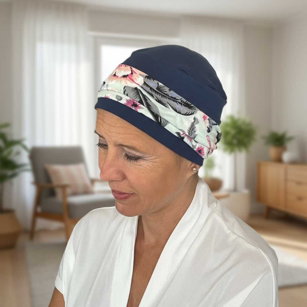 Woman wearing a floral patterned hat for cancer patients and navy cap in a home setting