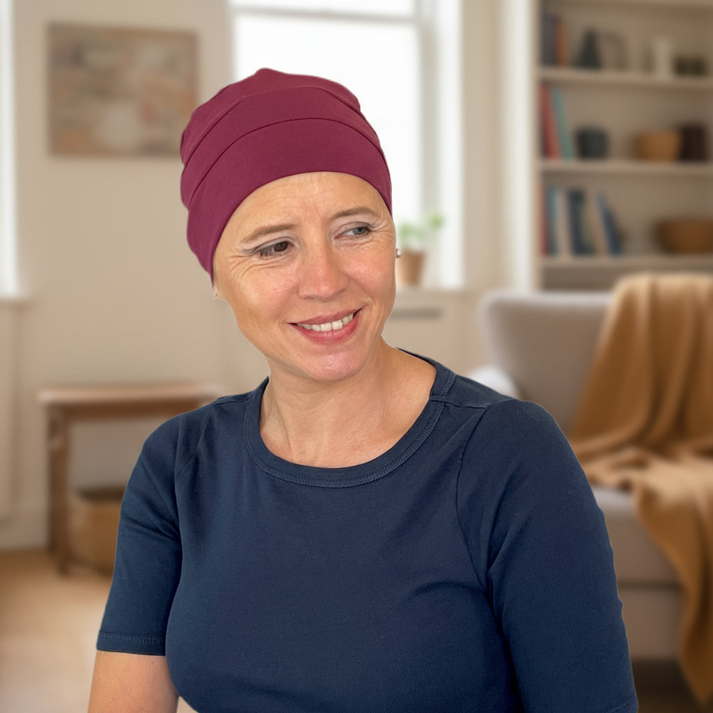 Woman wearing a maroon chemo sleep hat indoors in a home setting