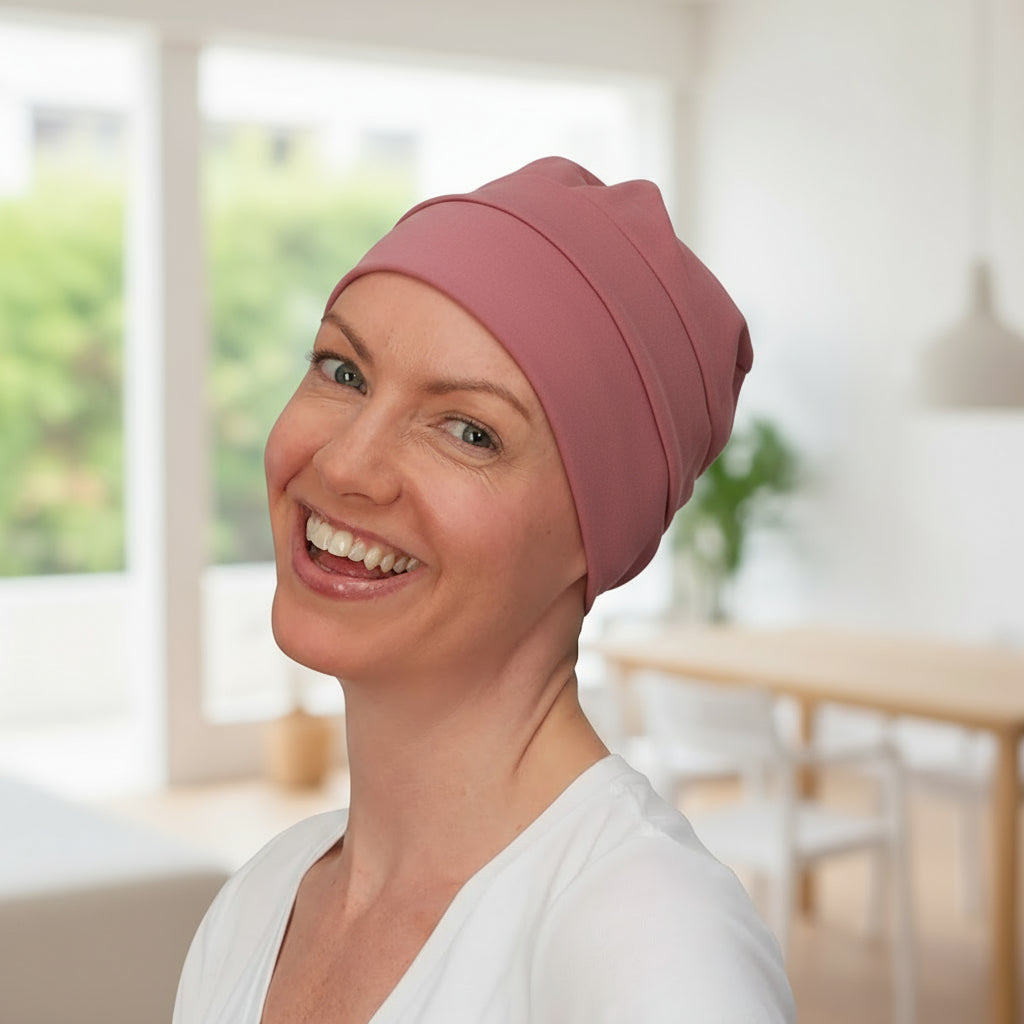Woman wearing a pink chemo hat in a bright, blurred indoor setting
