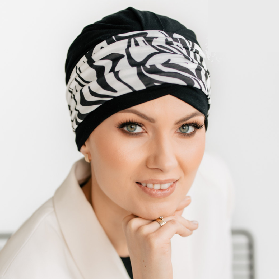 Woman wearing a black hat for cancer patients with white patterns on a plain background