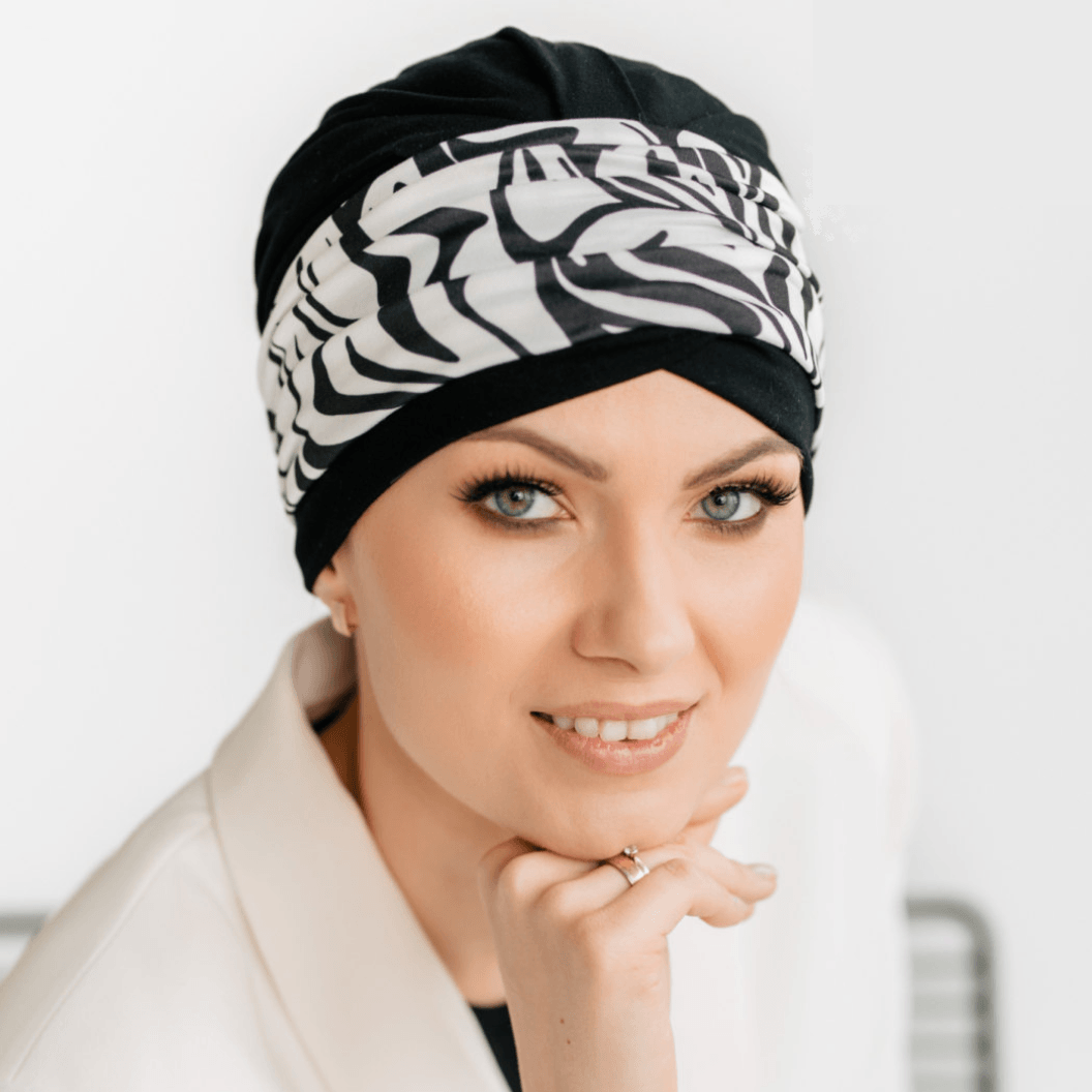 Woman wearing a black hat for cancer patients with white patterns on a plain background