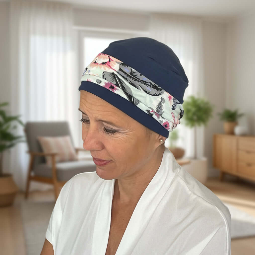 Woman wearing a floral patterned hat for cancer patients and navy cap in a home setting