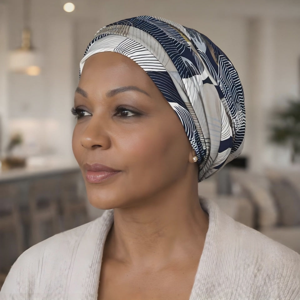 A woman wearing a chemo headscarf in blue, white and beige looking at the camera and smiling