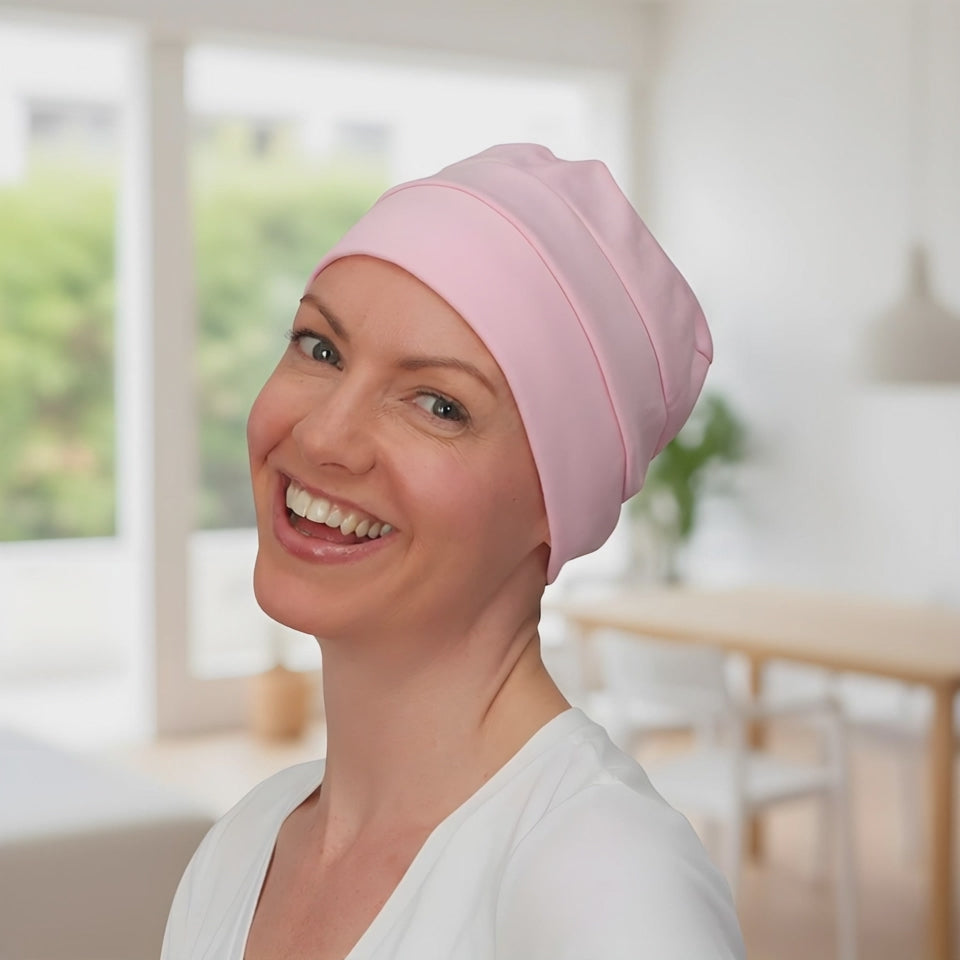 A woman wearing a chemo hat in pink looking at the camera and smiling